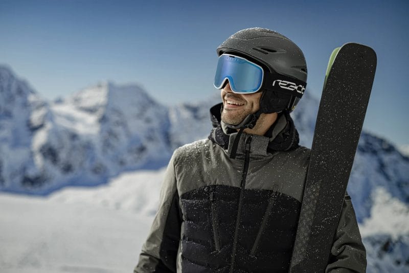 A guy in complete ski outfit wearing an Optrel React Sight 2.0 Ski Goggles with blue lens - image for React Products.