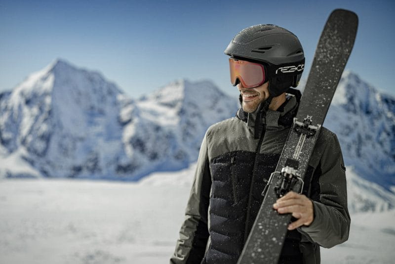 A guy in complete ski outfit wearing an Optrel React Sight 2.0 Ski Goggles with red lens - image for React Products.